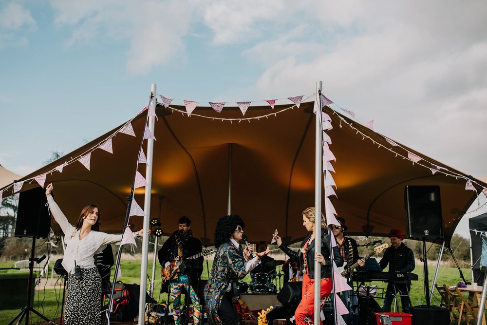 Festival wedding band playing under stretch tent with bunting and lighting and Team E dancing to the music at wild wedding venue elmore court