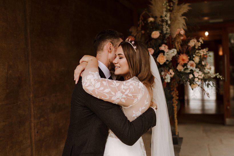 Bride and groom embracing outside of the Gillyflower at Elmore Court with flower arrangements in the background