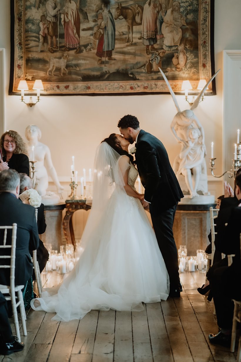 Bride and groom kissing ion the great hall at Elmore Court after saying I Do, with candles displayed on the floor