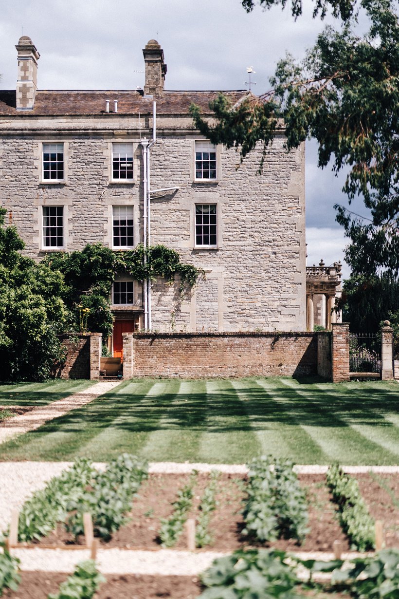 Stately home Elmore court as seen from the walled garden with organic seedlings growing and beautifully moved lawn stripes on the lawn beyond