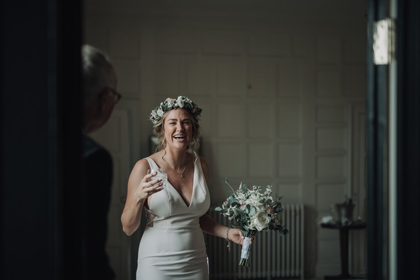 Happy bride laughs with bouquet and champagne wearing a flower crown on her micro wedding day during corona virus pandemic