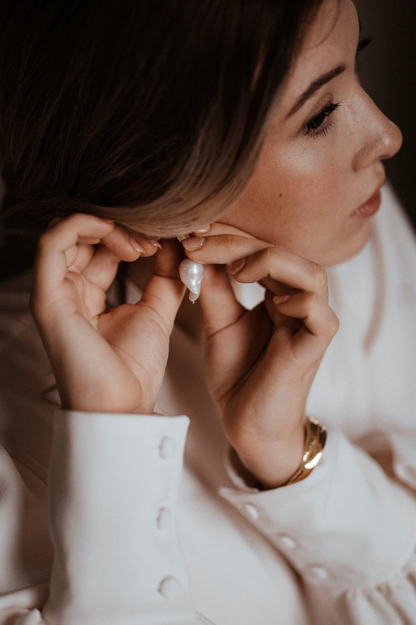 Girl with the pearl earring wedding inspiration bride in button cuffs doing up rough pearl earrings 