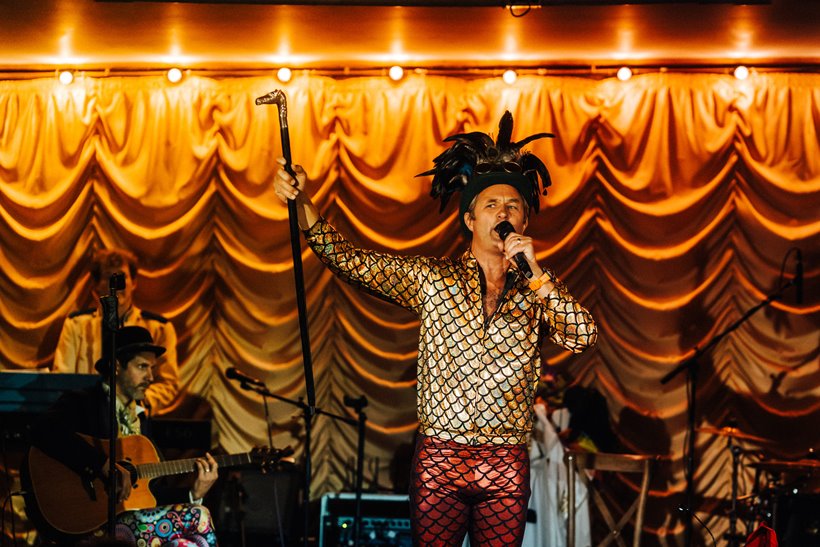 Front man dressed in gold against gold backdrop performs on stage for the pandemic cabaret parrot cage at elmore court