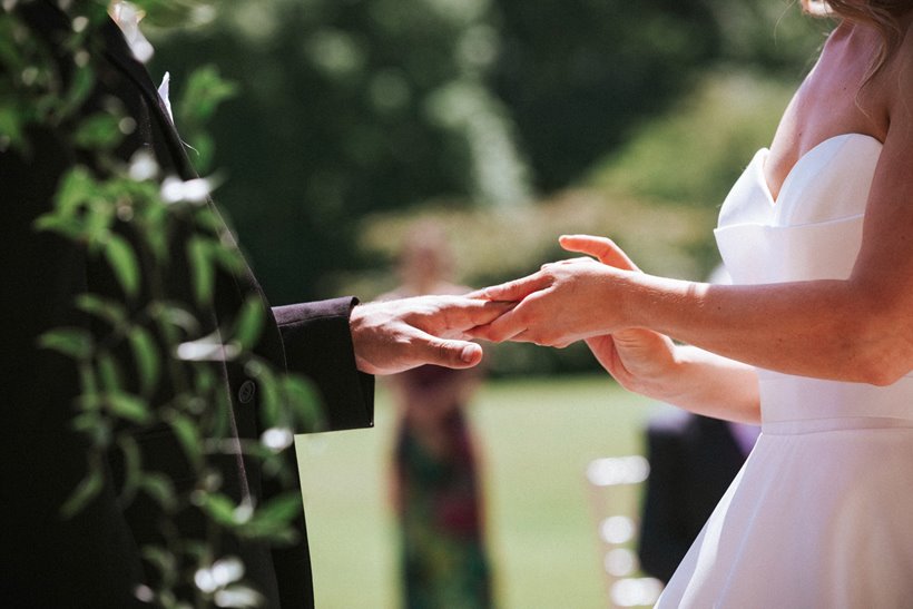 Bride and grooms hands as they exchange rings in their outdoor wedding ceremony at stately home elmore court