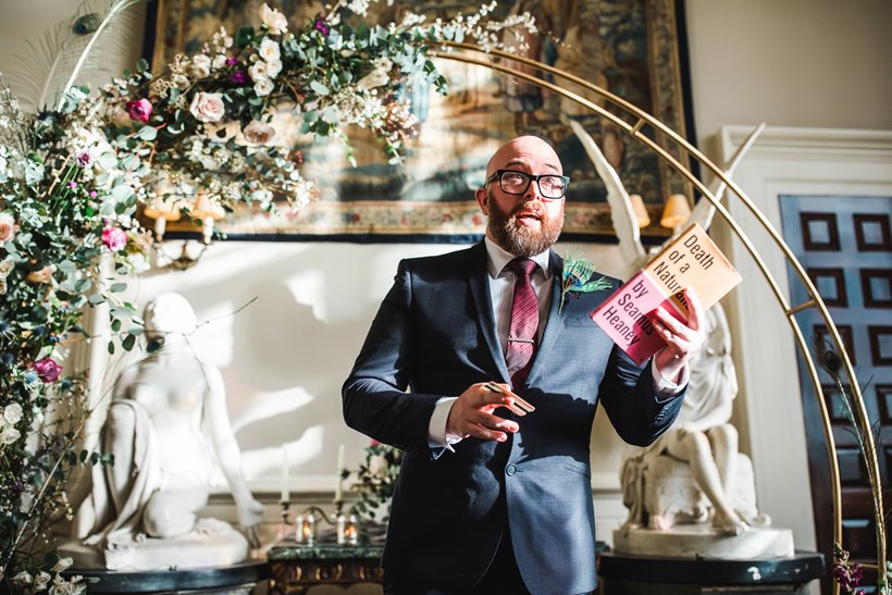 Guest poetry reading during wedding ceremony in front of floral arch for weekend wedding