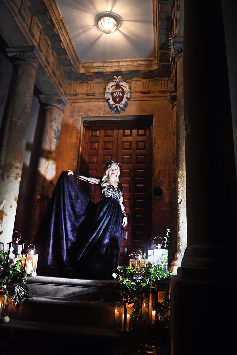 Bride in black wedding dress and autumn flower crown in candlelight on the steps of old mansion house wedding venue for her Halloween wedding