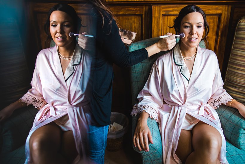 Bride having makeup applied in personalised dressing gown on morning of weekend long wedding